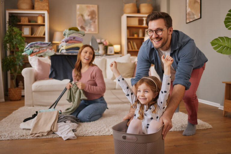 Little girl and dad laughing while playing with the laundry basket in living room